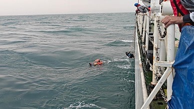 Fisherman in the water near a rescue boat off Mangaluru coast during a rescue operation.