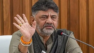 Karnataka CM D K Shivakumar speaking at a press conference with a raised hand gesture.
