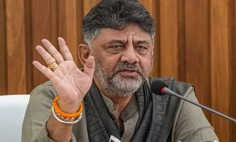 Karnataka CM D K Shivakumar speaking at a press conference with a raised hand gesture.