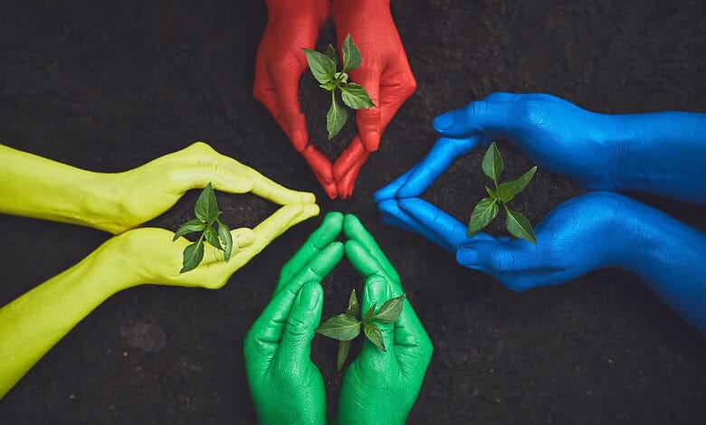 Protecting the environment with colourful hands holding small green plants for sustainability and eco-fri.