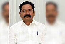 A man with a mustache wearing a white shirt, standing against a light background.
