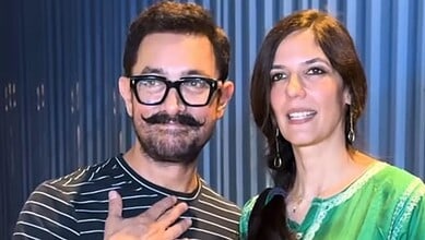 A man with glasses and a mustache smiling alongside a woman in a green dress at an indoor event.