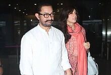 A man with glasses and a woman in a pink scarf walking through an airport terminal.