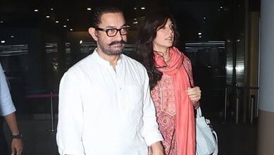 A man with glasses and a woman in a pink scarf walking through an airport terminal.