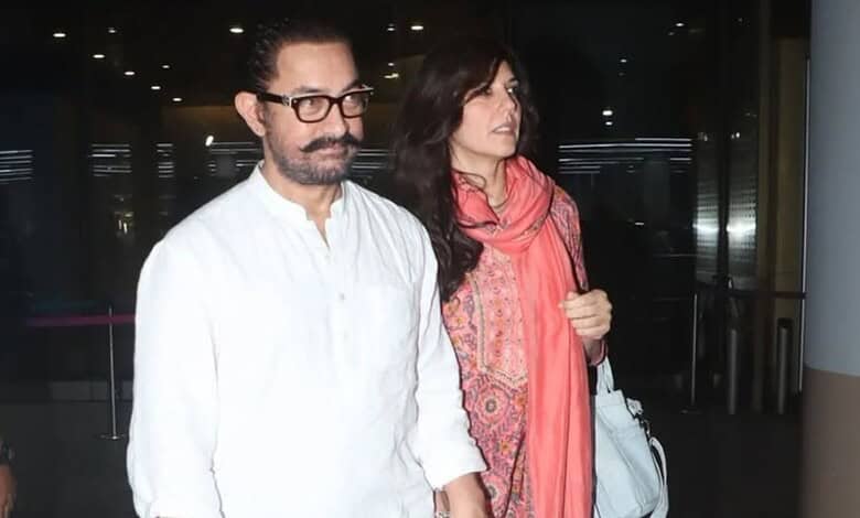 A man with glasses and a woman in a pink scarf walking through an airport terminal.