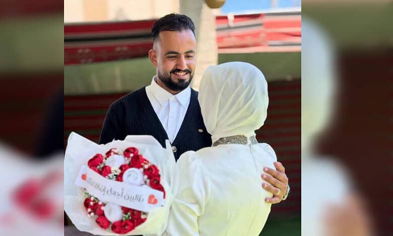 Smiling man in a black sweater hugging a woman in white with a headscarf.