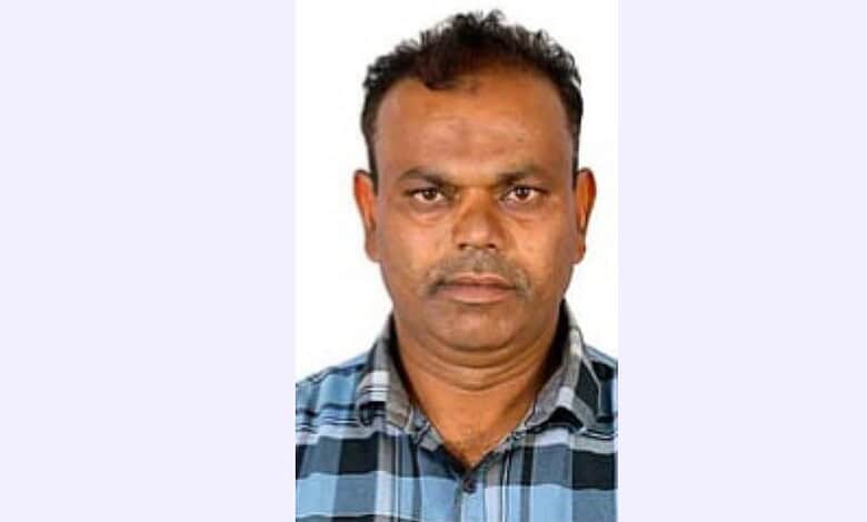 Man in a checkered shirt with a serious expression, facing the camera.