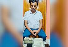 Man sitting with stacks of cash on table in indoor setting.