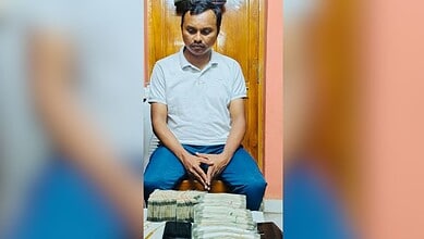 Man sitting with stacks of cash on table in indoor setting.