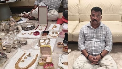 Antique silver jewelry displayed on a table with a man sitting on a sofa in the background.