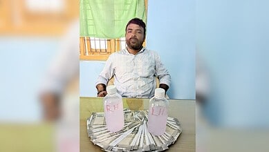 Man sitting at a table with two bottles and currency notes in front of him.