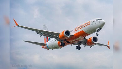 Airplane in flight with orange and white livery, under a cloudy sky, promoting new flight route.
