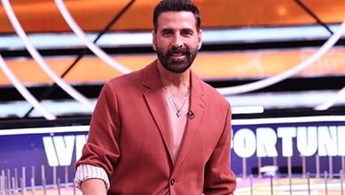A man with a beard wearing a brown blazer and white shirt, smiling in a modern studio setting.