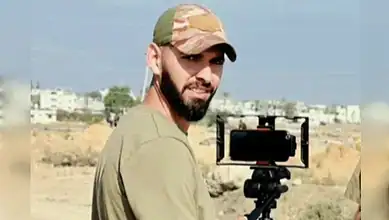 Al Jazeera cameraman Ahmed Washah stands outdoors beside filming equipment in the Gaza Strip.
