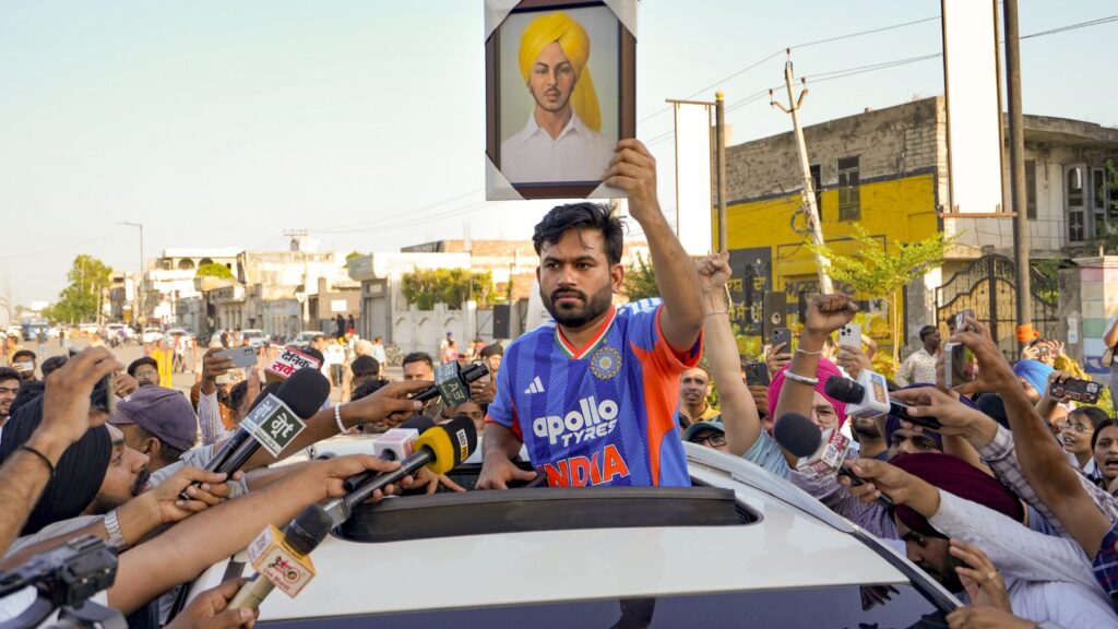 A man holding a portrait of a Sikh leader during a public rally in India, surrounded by media and support.