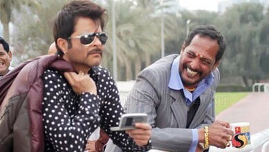Akshay Kumar in a polka dot shirt and sunglasses, with a man in a suit smiling and holding a mug.
