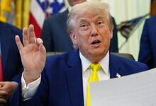 Donald Trump speaking and gesturing with his hand during a press event, surrounded by officials in the Wh.