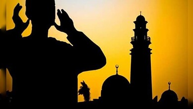 Silhouette of a person reciting the Azaan beside a mosque at sunset.