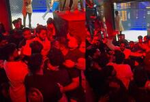 A group of people gathered at an indoor event with a stage and large screen, engaging in conversation and.