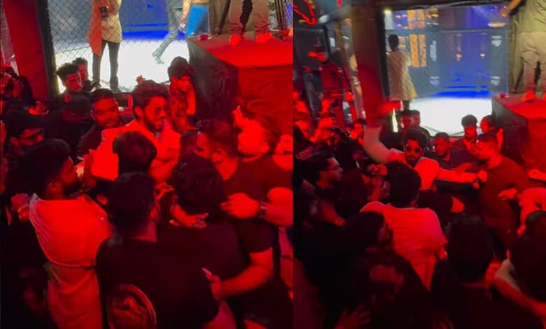 A group of people gathered at an indoor event with a stage and large screen, engaging in conversation and.