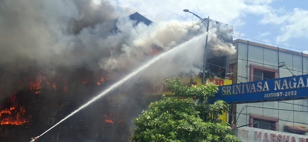 Firefighters battling a large blaze at Srinivasa Nagar, with thick smoke and flames engulfing the buildin.