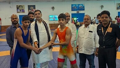Young wrestlers and officials at a wrestling event in an indoor sports arena.