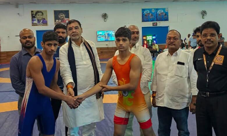 Young wrestlers and officials at a wrestling event in an indoor sports arena.