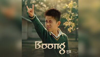 Young boy in a green sweater making a rock hand sign outdoors.