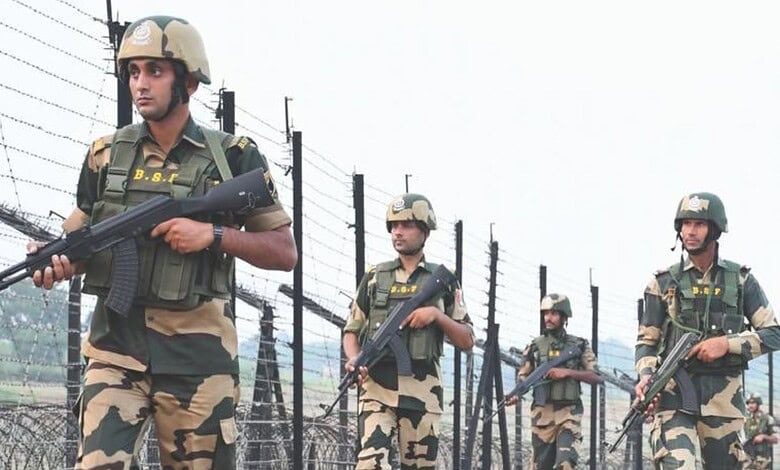 Indian paramilitary soldiers patrolling along a barbed wire fence, equipped with rifles and protective ge.