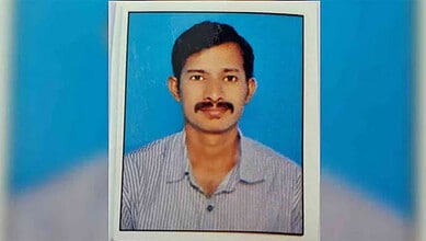 Portrait of a man with a mustache wearing a striped shirt, set against a blue background.