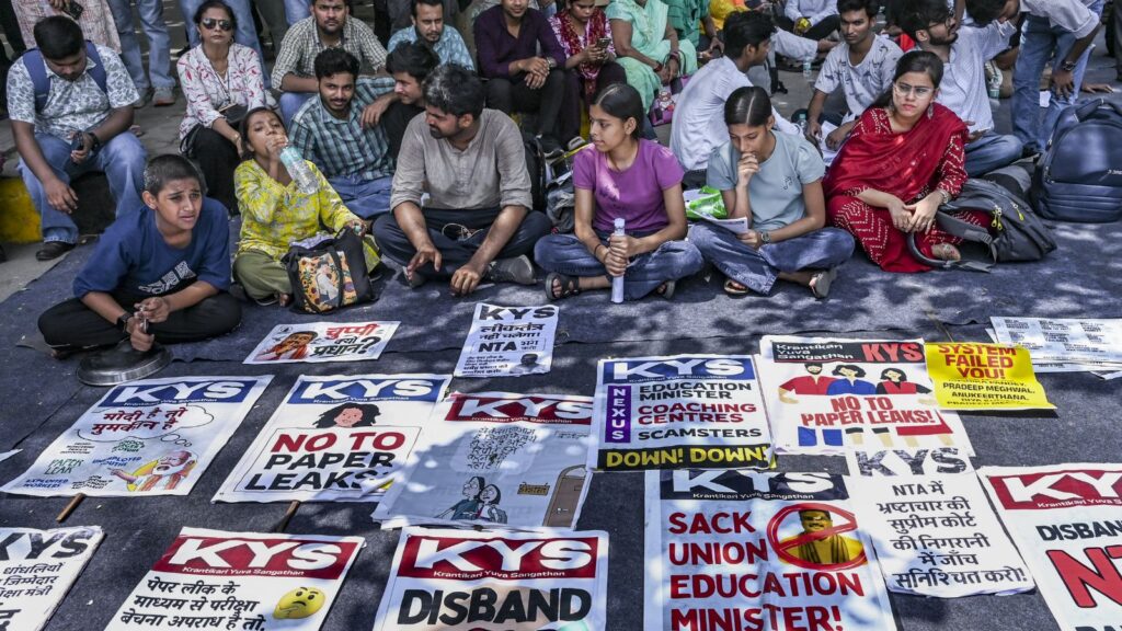 Protesters sitting on the ground with banners against paper leaks and education issues.