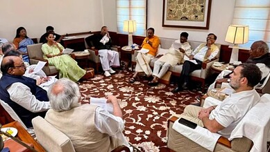 Group of politicians and officials in a formal discussion in a well-lit living room.