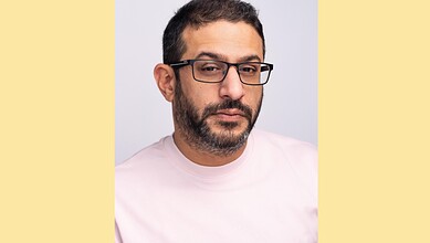 Portrait of a man with glasses and a beard, wearing a light pink shirt, looking at the camera.