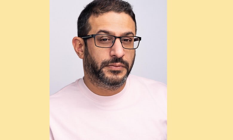 Portrait of a man with glasses and a beard, wearing a light pink shirt, looking at the camera.
