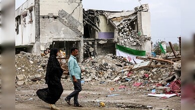 People walking past destroyed buildings and debris after an earthquake.