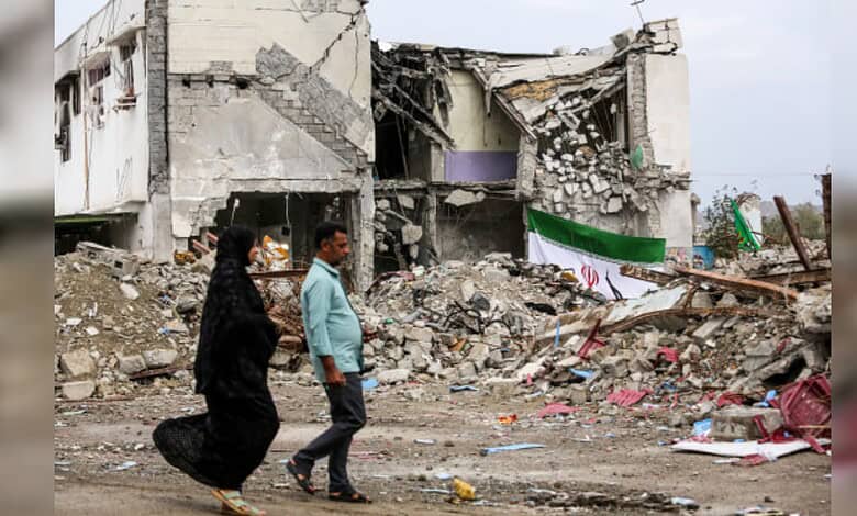 People walking past destroyed buildings and debris after an earthquake.