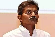 Indian politician with mustache in white shirt during a public event, serious expression.