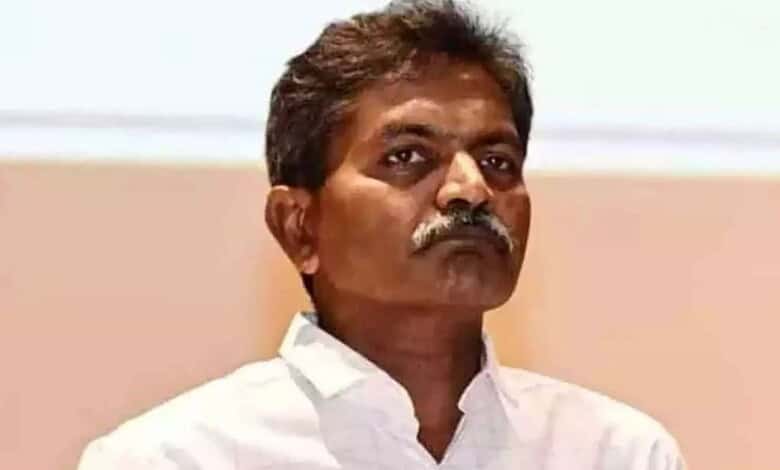 Indian politician with mustache in white shirt during a public event, serious expression.