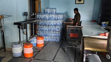Worker checks bottled water stock at water unit in Hyderabad amid safety concerns.