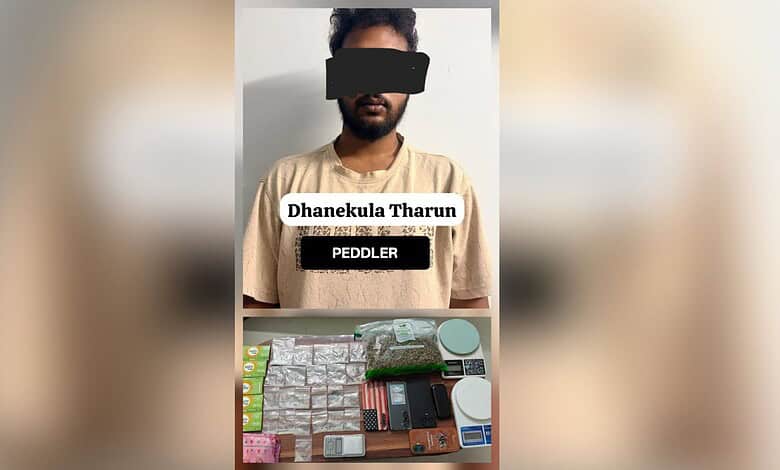 A man with a black bar over his eyes standing behind a table with drugs and paraphernalia.