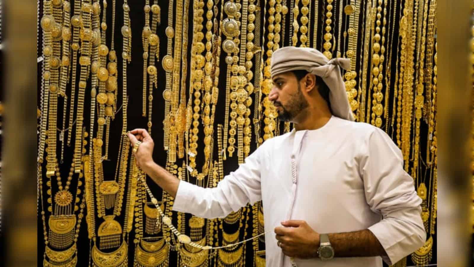 Man examining gold necklaces in a vibrant jewellery market.