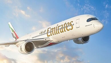 Emirates Airbus A350-900 aircraft flying against a blue sky with clouds.