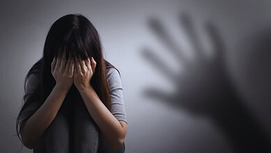 A woman with long dark hair covering her face, appearing distressed or upset, in a dimly lit room.