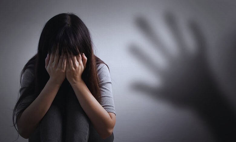 A woman with long dark hair covering her face, appearing distressed or upset, in a dimly lit room.