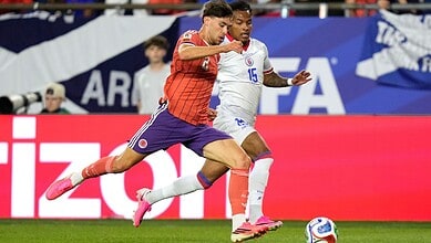A football match scene with two players competing for the ball, one in a red jersey and the other in a wh.