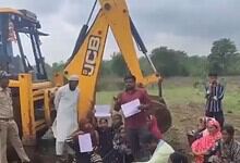 Farmers lying on ground with excavator and forest officials nearby during protest in India.