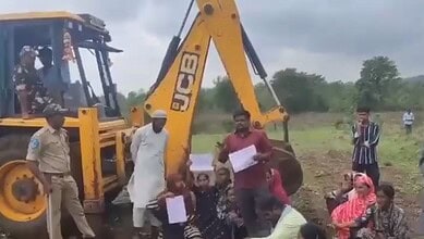 Farmers lying on ground with excavator and forest officials nearby during protest in India.