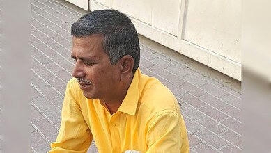 Man in yellow shirt sitting on sidewalk with a contemplative expression.