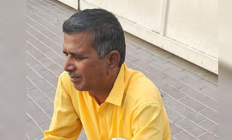 Man in yellow shirt sitting on sidewalk with a contemplative expression.