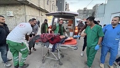 Medical workers transport a Gaza cancer patient on a stretcher outside a hospital beside an ambulance.